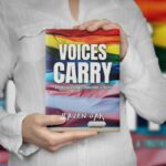 Voices Carry: A Story of Teaching, Transitions, & Truths by Raven Oak. Book is being held by a woman in a white shirt. The cover is a pride flag transitioning into a transgender pride flag with the title.
