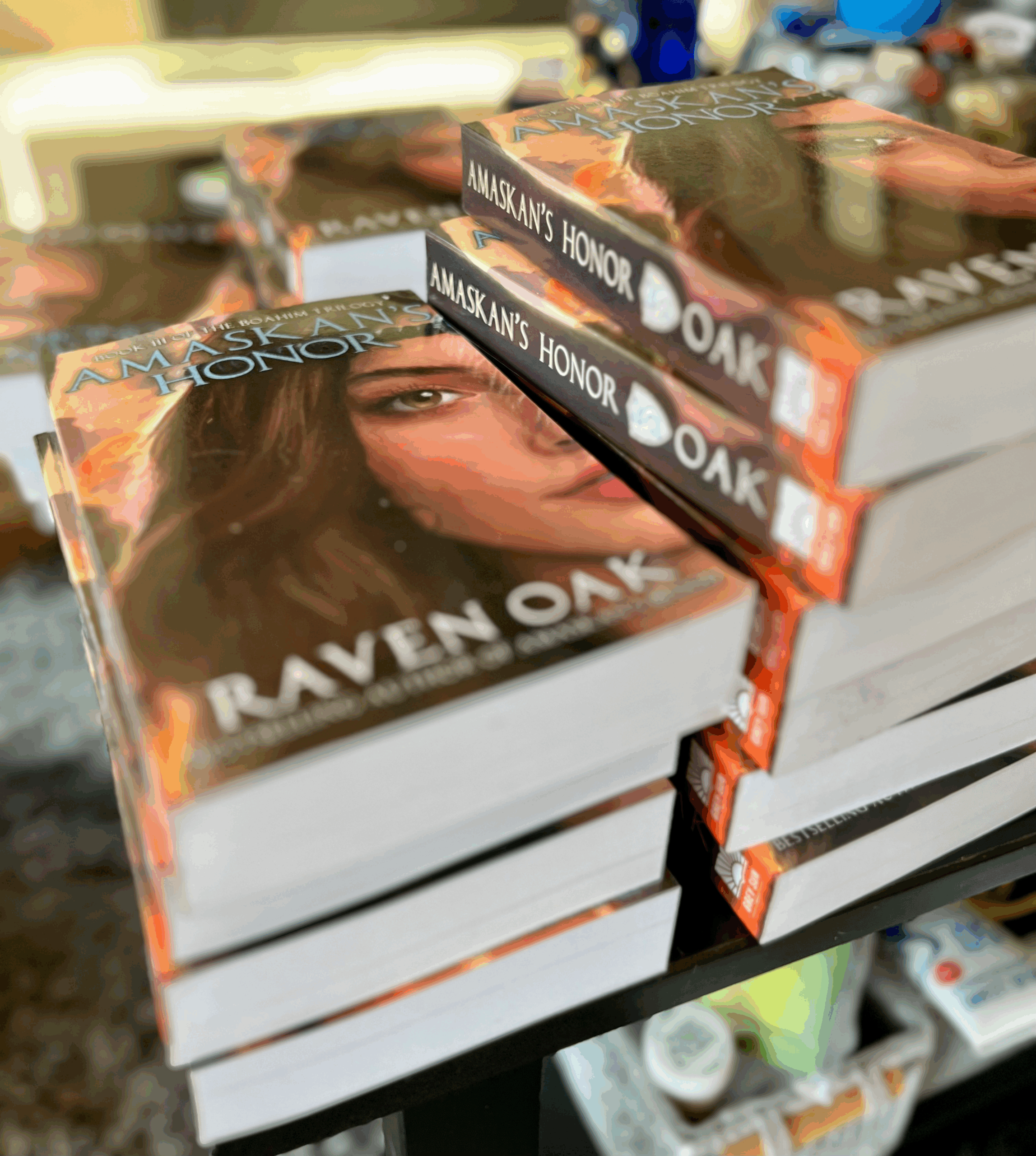 Two stacks of books are sitting on the table. The books are copies of Amaskan's Honor by Raven Oak and are thick paperbacks.